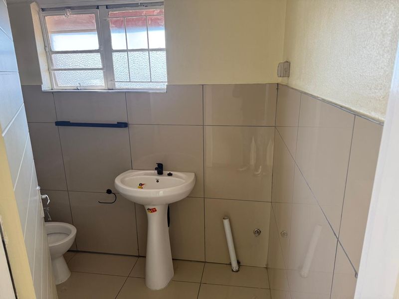 A functional bathroom featuring a pedestal basin, toilet, and neutral wall tiling, requiring minor finishing touches to the plumbing and wall paint.