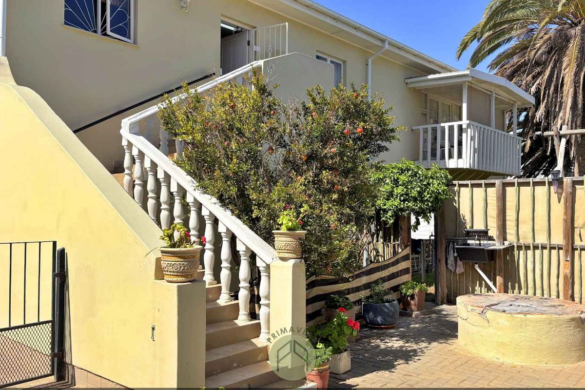 Rear exterior view featuring a paved courtyard, concrete staircase with balustrades, and access to upper level balcony.