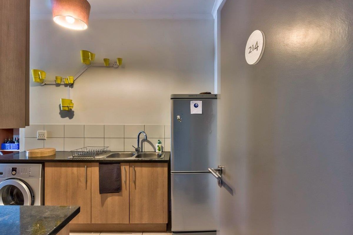 A compact kitchen area featuring wooden cabinetry, a stainless steel sink, tiled splashback, and an integrated washing machine.