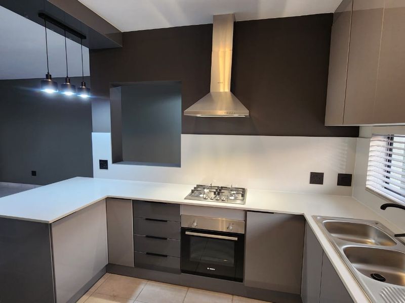 Modern kitchen featuring sleek grey cabinetry, quartz countertops, built-in oven, gas hob, stainless steel extractor fan, and a double bowl sink.