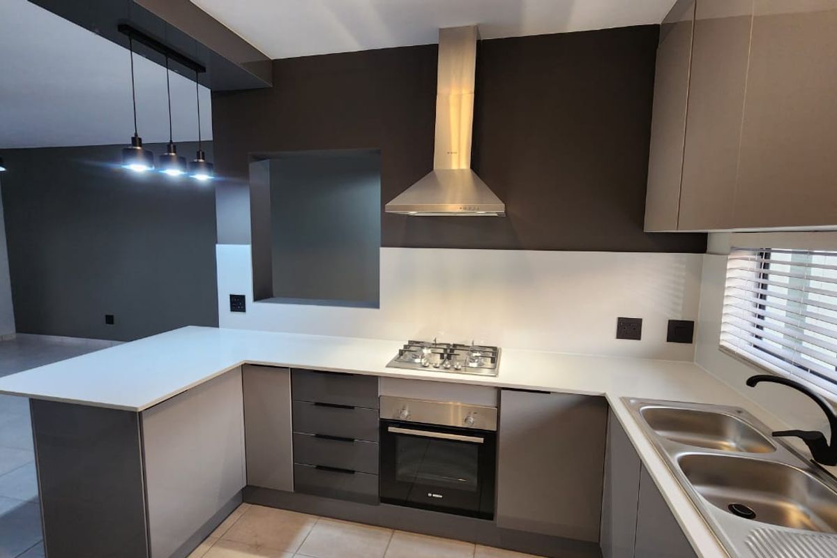 Modern kitchen featuring sleek grey cabinetry, quartz countertops, built-in oven, gas hob, stainless steel extractor fan, and a double bowl sink.