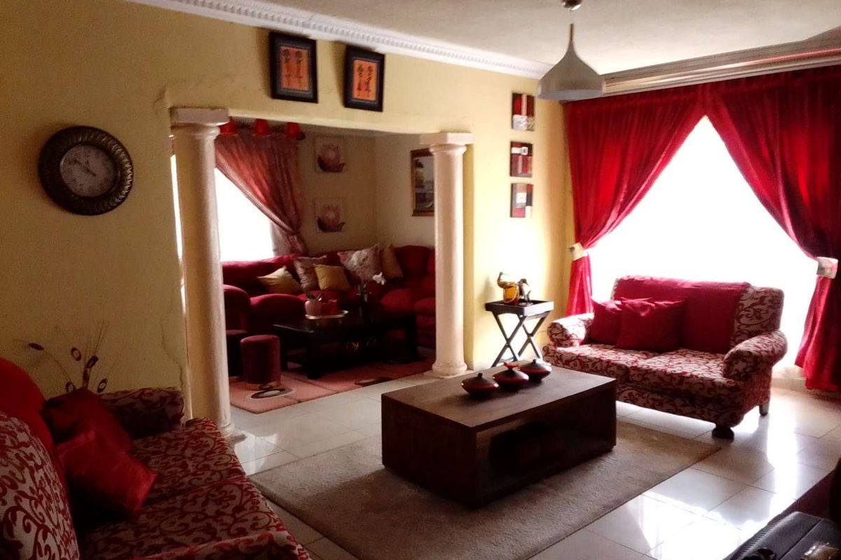 A living room featuring decorative columns, tiled flooring, and large windows with red curtains, creating a distinct partitioned seating area.