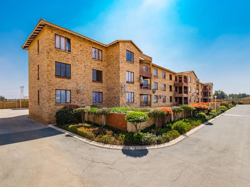 Exterior view of a multi-story face brick apartment complex featuring balconies, paved driveway access, and established garden landscaping.