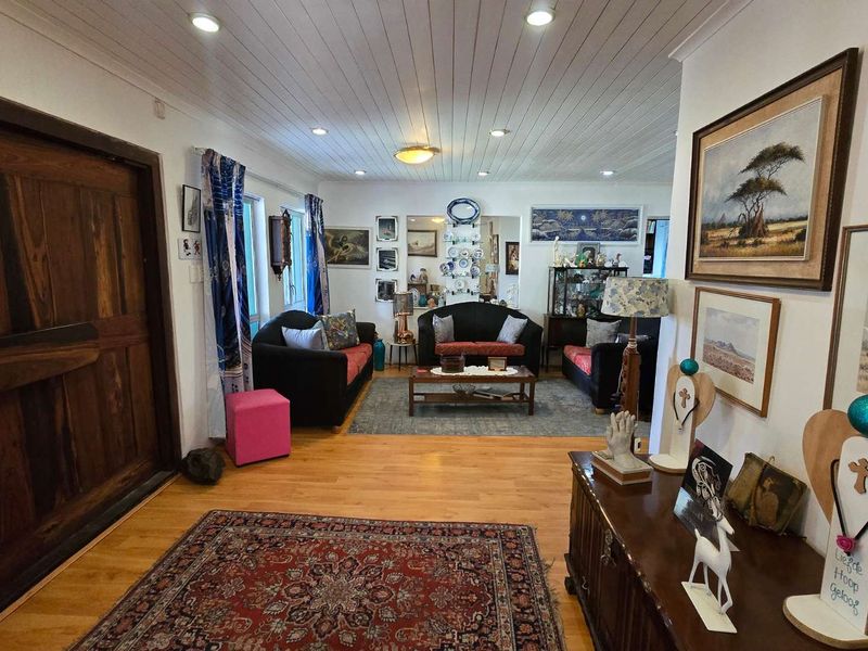 Spacious living room featuring timber flooring, a large solid timber entrance door, and a white tongue and groove ceiling with recessed lighting.
