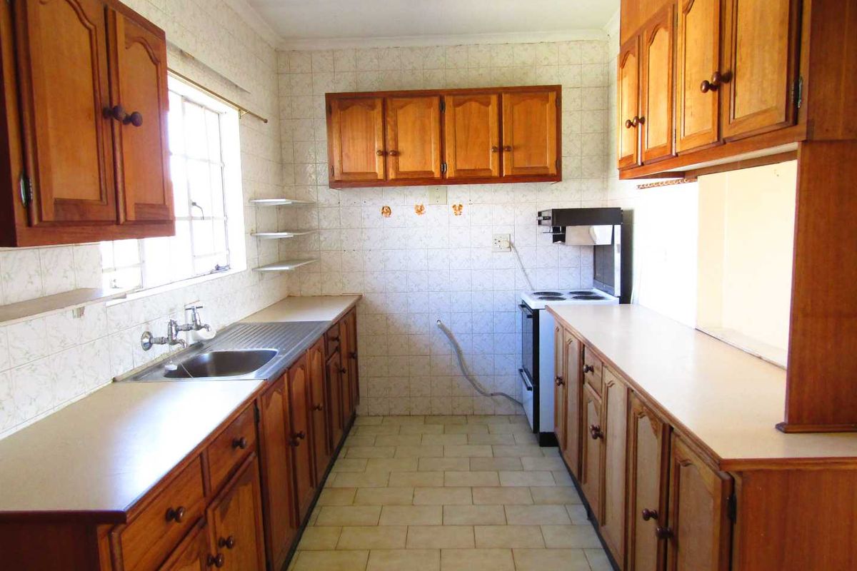 A functional galley-style kitchen featuring original wooden cabinetry, laminate countertops, and tiled finishes, offering a blank canvas for modern renovation.