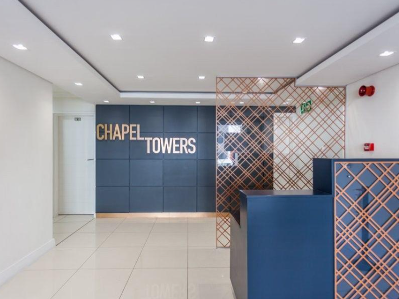 Modern apartment building entrance lobby featuring a reception desk, tiled flooring, recessed lighting, and decorative metal screening.