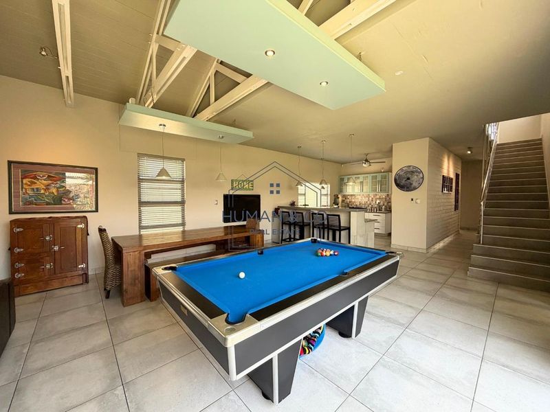 Spacious open-plan living area featuring exposed timber trusses, tiled flooring, a modern staircase, and an integrated kitchen with a central island.