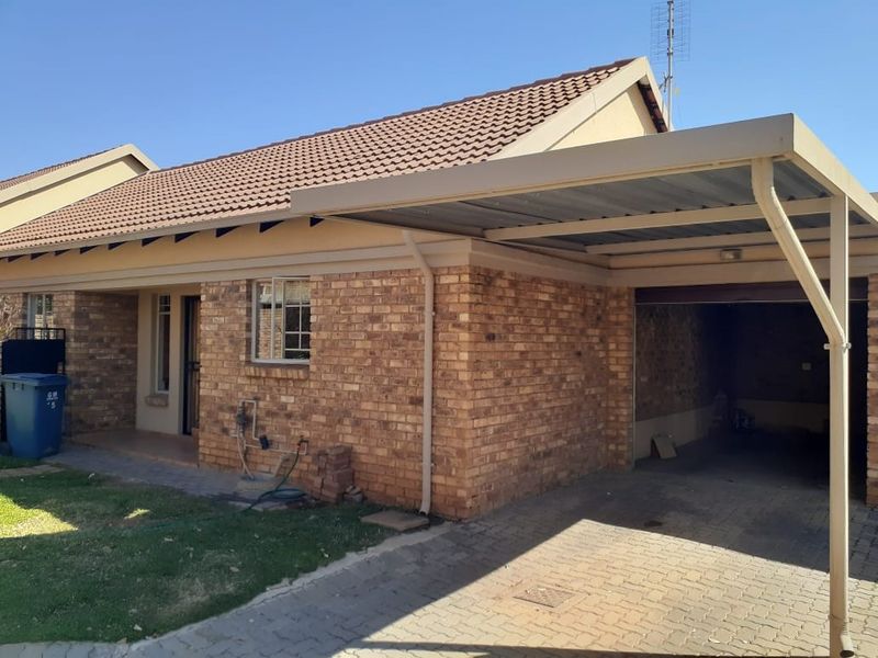 Front exterior view of a face brick apartment featuring a tiled roof, a paved driveway, and a covered carport.