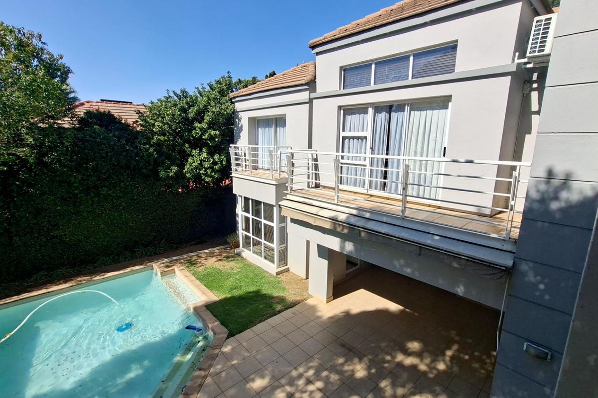 Rear view of the townhouse featuring a tiled patio, swimming pool, and an upper-level balcony with metal railings.