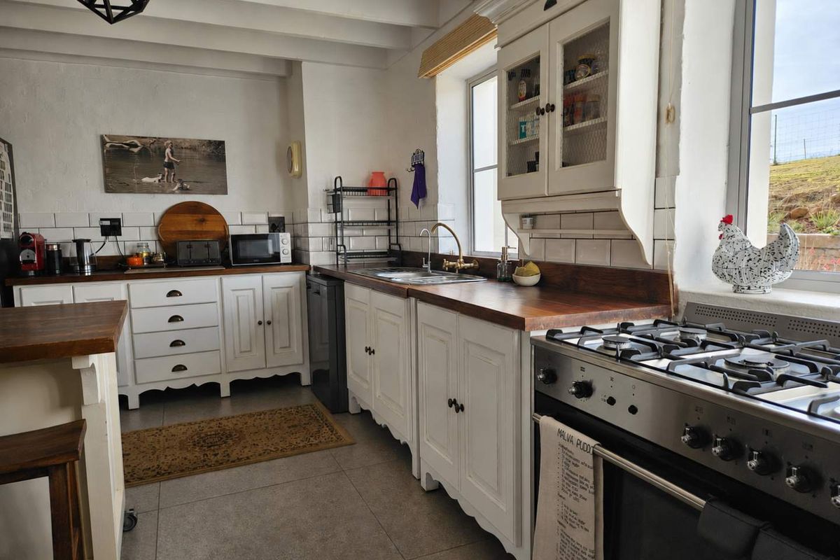 A charming country-style kitchen featuring white cabinetry, wooden countertops, a stainless steel gas stove, and subway tile backsplash with exposed ceiling beams.