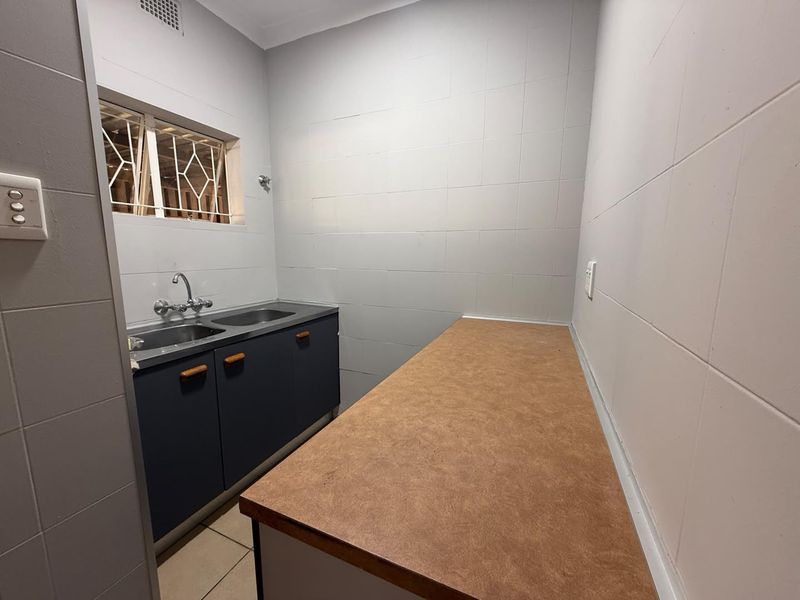 A functional laundry room featuring tiled walls, a double stainless steel sink with cabinetry, and a spacious laminate countertop for workspace.