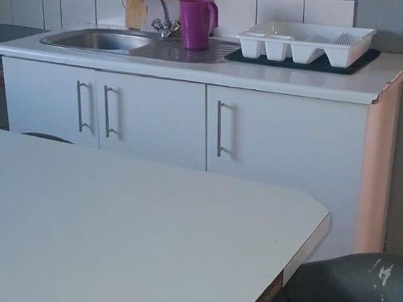 A compact kitchen area featuring a stainless steel sink, tiled splashback, and white base cabinetry with visible signs of wear.