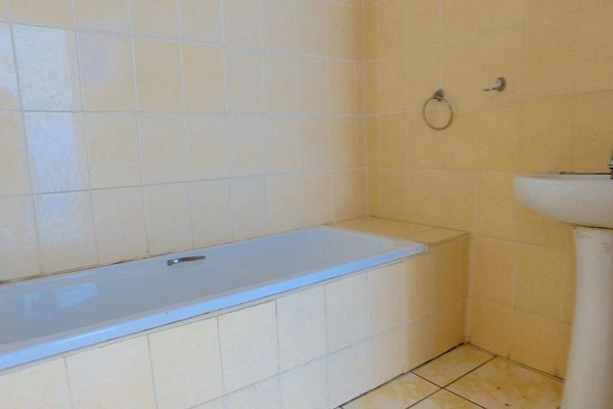 A dated bathroom featuring a built-in bathtub and a pedestal washbasin with yellow wall and floor tiling.