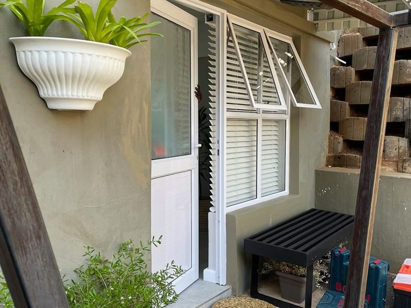 A small outdoor patio area featuring a uPVC door and window, with concrete flooring and a retaining wall structure.