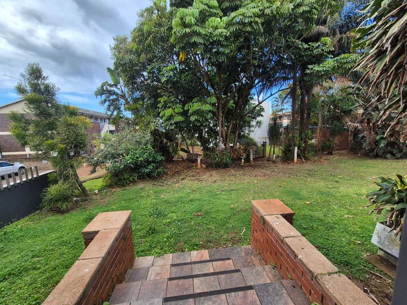 A private garden area featuring a lawn, mature trees, and brick-edged tiled steps leading down to the outdoor space.