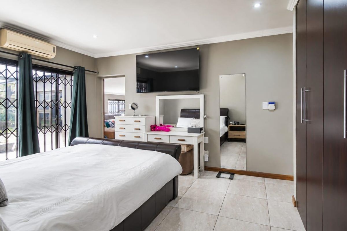 Spacious bedroom featuring tiled flooring, built-in cupboards, recessed lighting, and a wall-mounted air conditioning unit with access to an outdoor area via security gates.