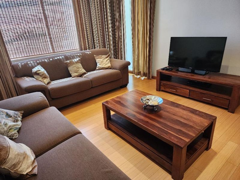 A comfortable living room featuring light-toned laminate flooring and large windows with full-length curtains, providing a bright and inviting atmosphere.
