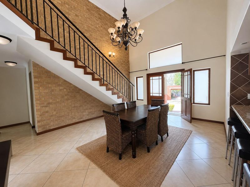 Spacious open-plan dining area featuring high ceilings, an exposed brick feature wall, a grand staircase, and direct access to the exterior.
