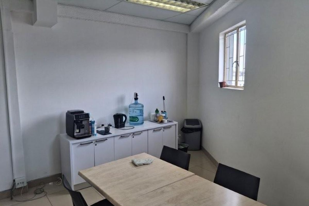 A functional office space featuring tiled flooring, a suspended ceiling with recessed lighting, and a window with security bars.
