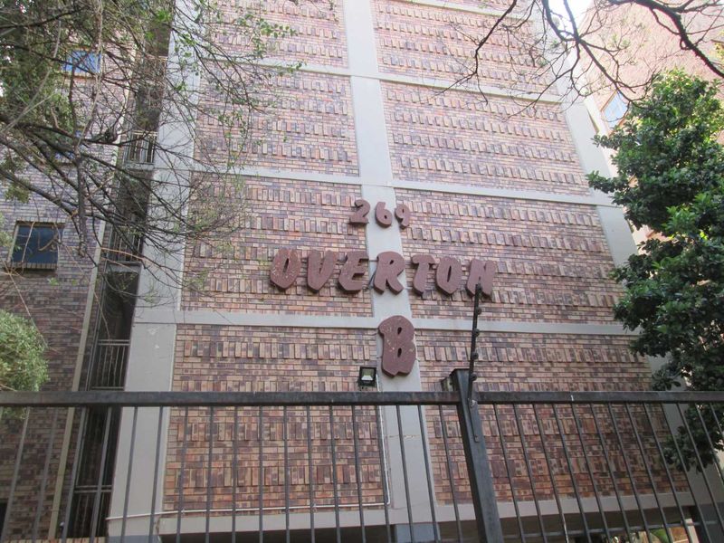Front facade of the Overton apartment building featuring brick construction and secure perimeter fencing.