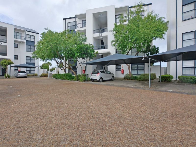 Exterior view of a modern apartment complex featuring paved parking areas with shade cloth carports and multi-story residential building facades.
