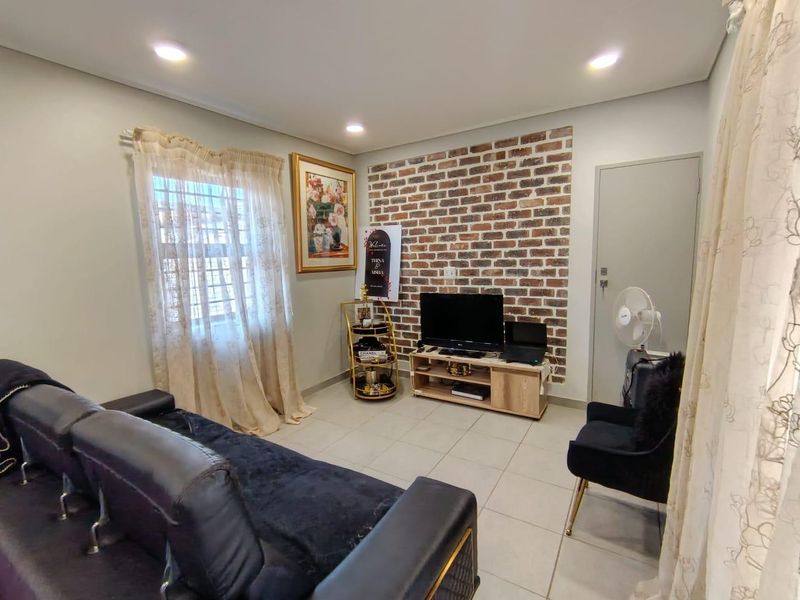 A cozy living room featuring a decorative exposed brick accent wall, neutral tiled flooring, and recessed ceiling lighting.
