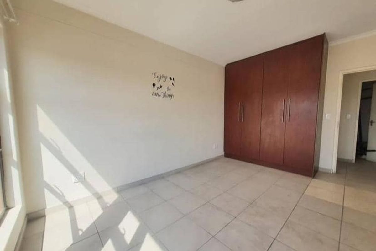 A bright bedroom featuring neutral floor tiles and a large, built-in dark wood wardrobe providing ample storage space.