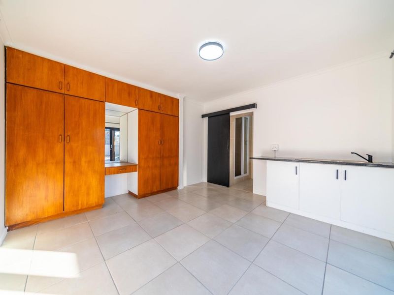 An open-plan living space featuring tiled flooring, extensive built-in wooden cabinetry with a vanity mirror, and a compact kitchenette area.