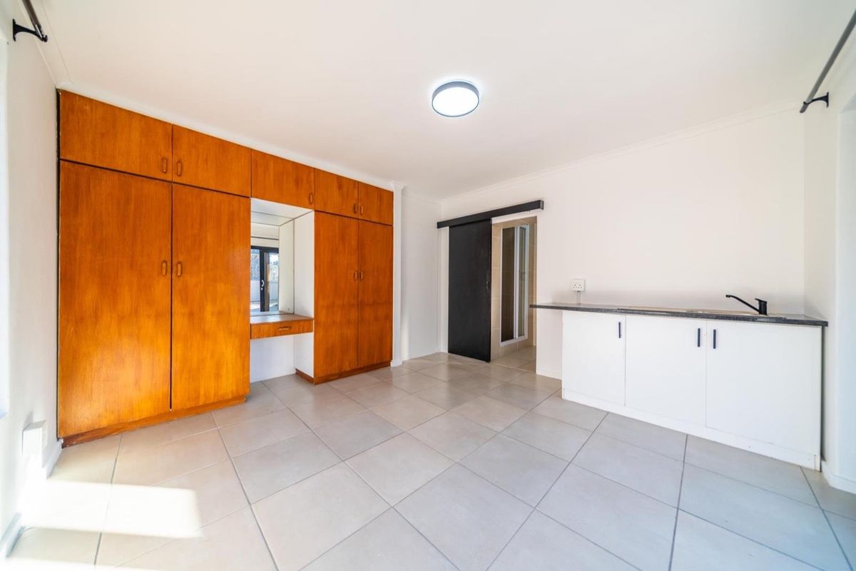 An open-plan living space featuring tiled flooring, extensive built-in wooden cabinetry with a vanity mirror, and a compact kitchenette area.