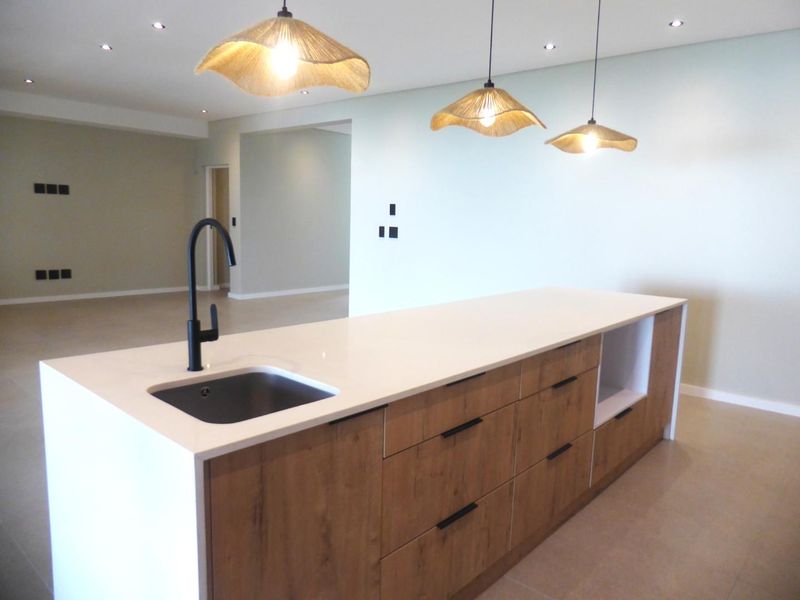 Modern kitchen island featuring a stone countertop, undermount sink, matte black faucet, and wood-finish cabinetry in an open-plan living space.