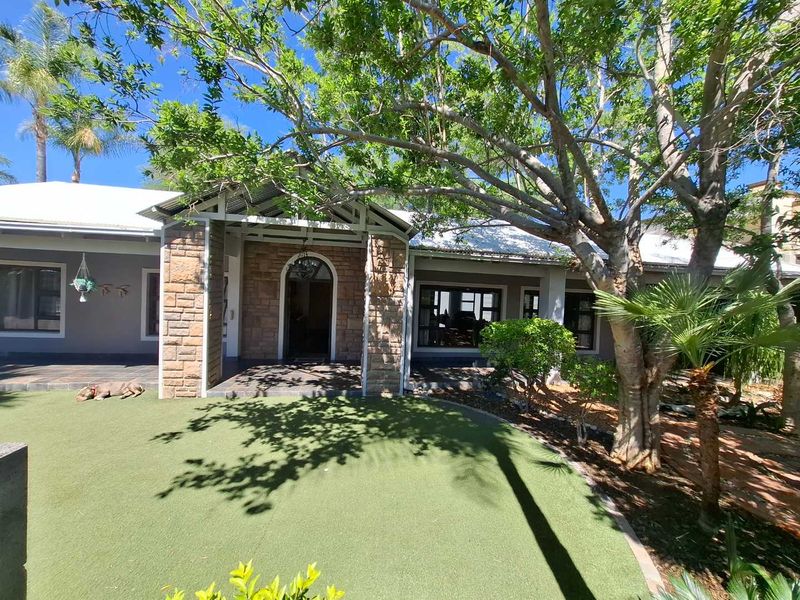 Front facade of the house featuring stone cladding, a covered entrance porch, and a well-maintained artificial lawn area.