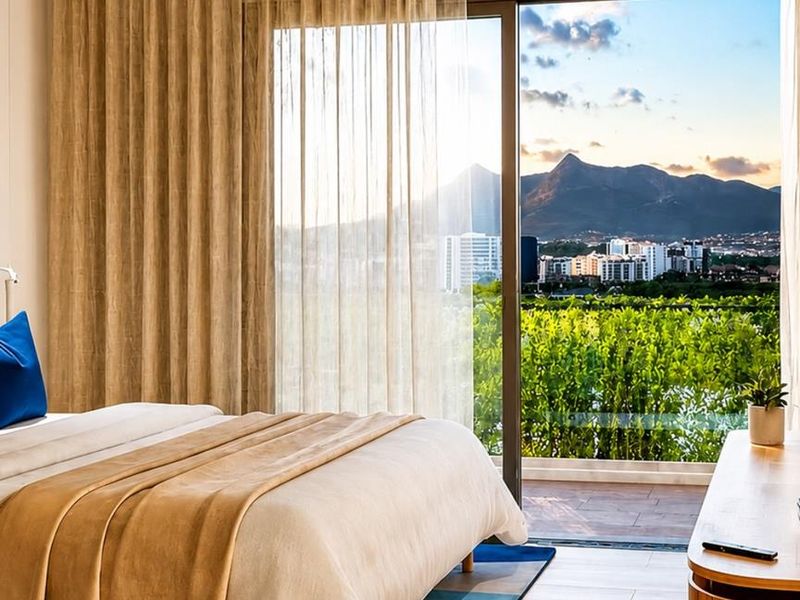 A bright bedroom featuring large sliding glass doors that open to a balcony with scenic mountain and city views.