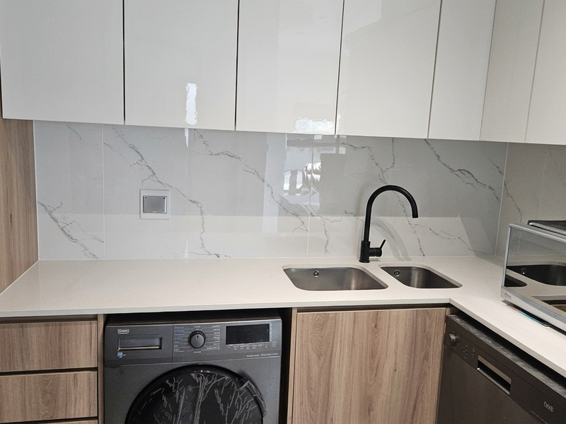 Modern kitchen featuring high-gloss cabinetry, stone countertops, marble-effect splashback, and integrated appliances including a washing machine and dishwasher.