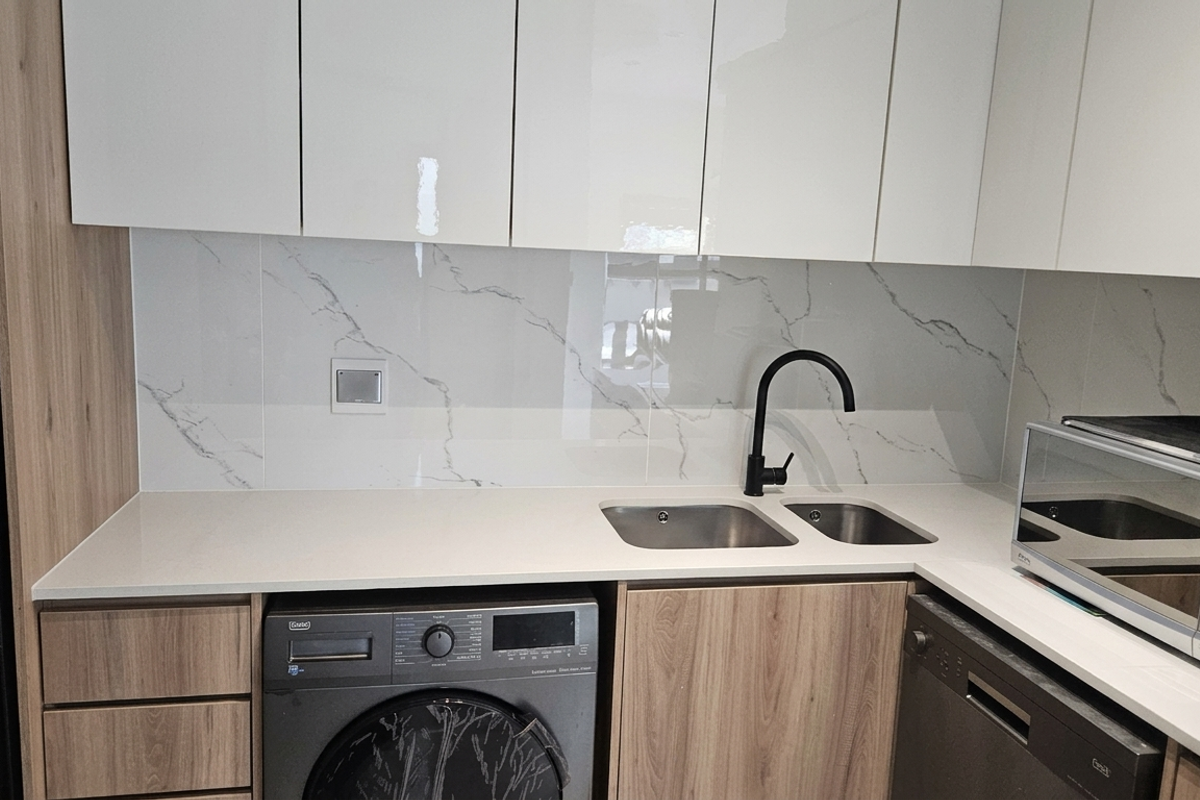 Modern kitchen featuring high-gloss cabinetry, stone countertops, marble-effect splashback, and integrated appliances including a washing machine and dishwasher.