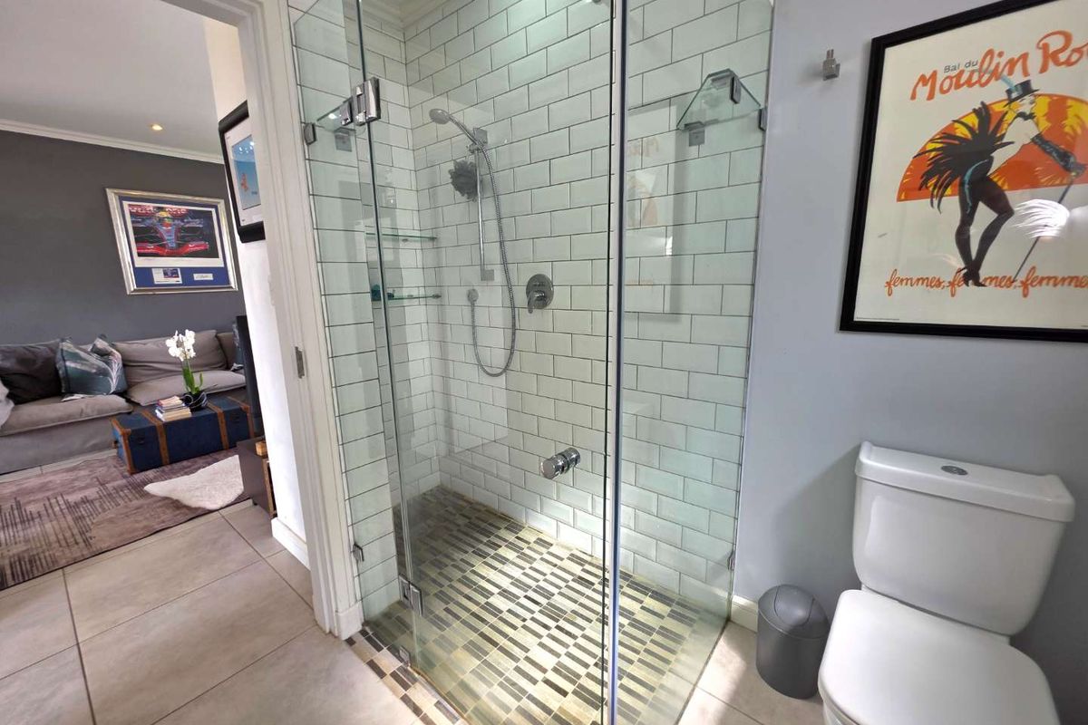 Modern bathroom featuring a glass-enclosed shower with subway tiling, mosaic floor accents, rainfall shower head, and a standard toilet.