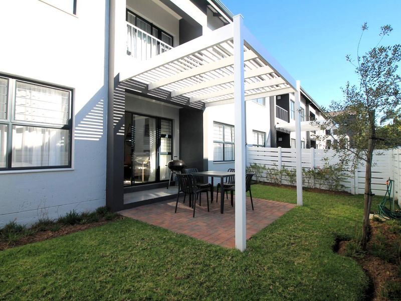 A well-maintained rear garden featuring a paved patio area with a modern white pergola, lawn, and secure perimeter fencing.
