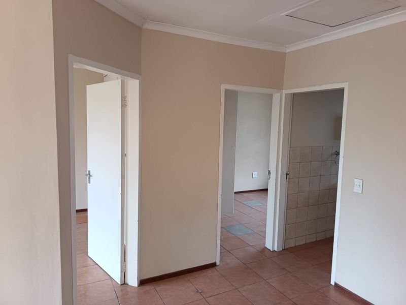 A neutral-toned hallway featuring tiled flooring and multiple doorways leading to adjacent rooms, providing a clean and functional transition space within the apartment.