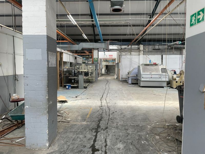 Industrial warehouse space featuring exposed steel trusses, concrete flooring, and functional ventilation systems, suitable for manufacturing or storage operations.