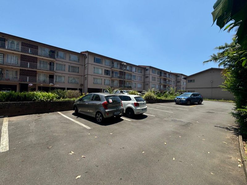 Exterior view of a multi-story apartment complex featuring an asphalt parking area and brick retaining wall.