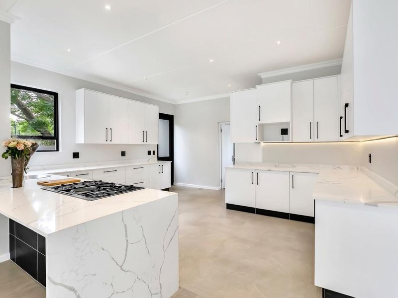 Modern, bright kitchen featuring white cabinetry, marble-look stone countertops, a central island with a gas hob, and sleek under-cabinet lighting.