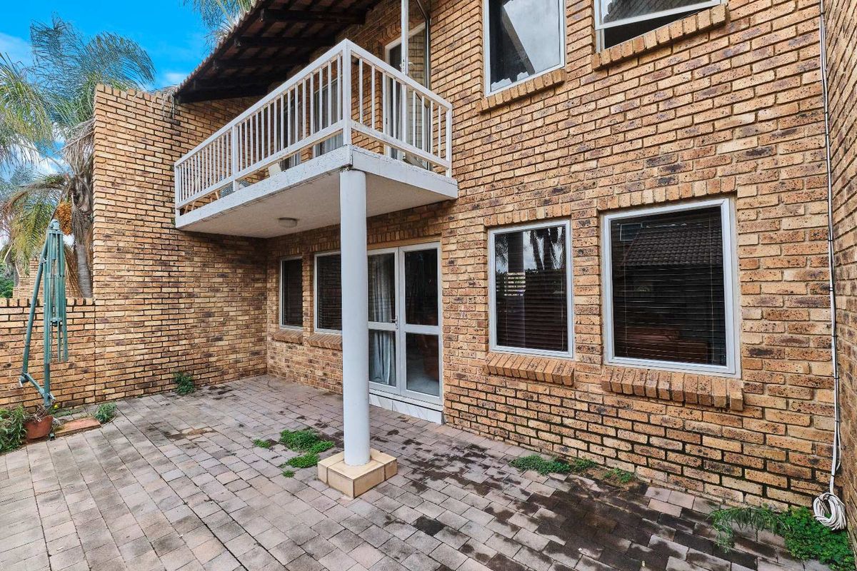 Rear view of the townhouse featuring a paved patio area, a raised balcony with white railing, and exposed brick facade.