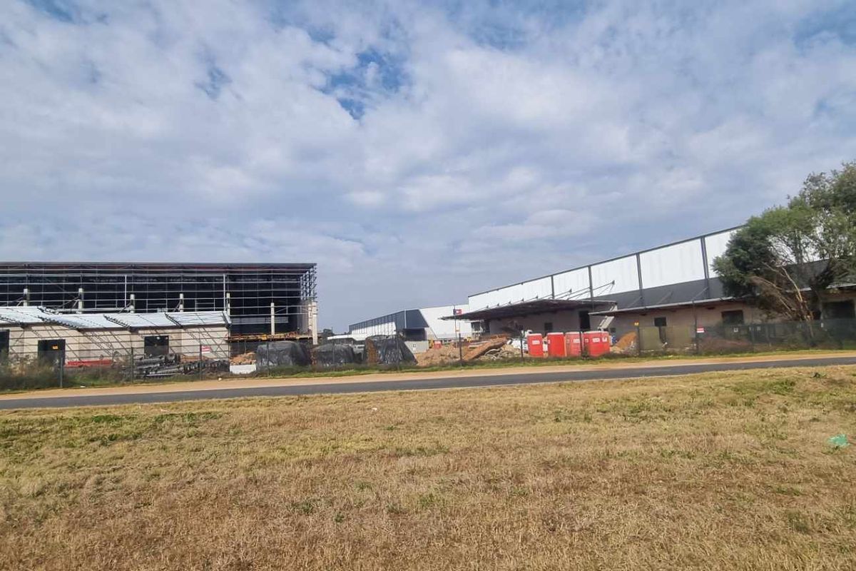 View of an industrial property development site featuring large warehouse structures under construction with exposed steel framing and surrounding open land.