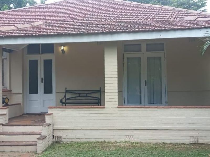 A charming single-story home featuring a covered front veranda, classic brick pillars, a tiled roof, and a prominent bay window.