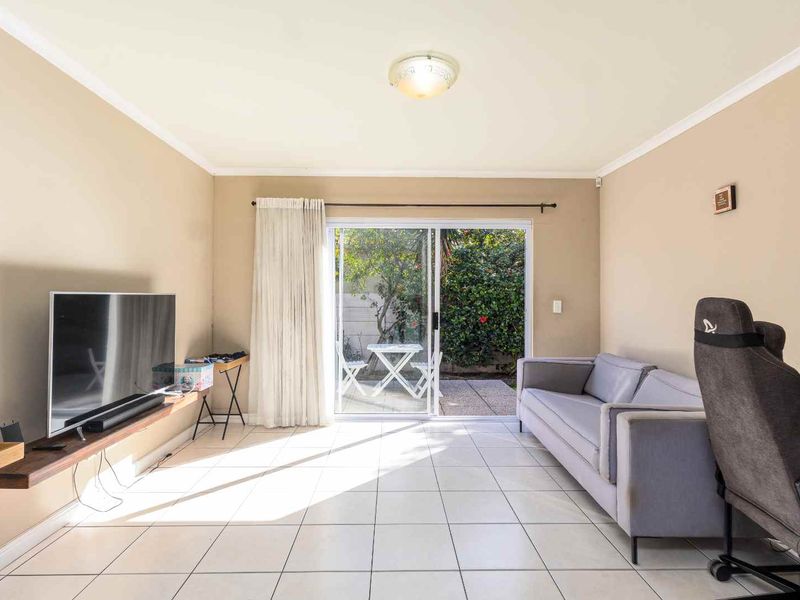 A bright living room featuring ceramic floor tiles, a coved ceiling, and a large sliding glass door providing direct access to the outdoor patio area.