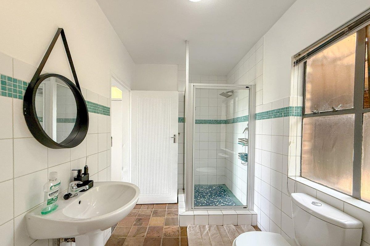 A functional bathroom featuring a pedestal washbasin, a tiled shower enclosure, and a toilet, finished with classic white wall tiles and terracotta-style floor tiles.