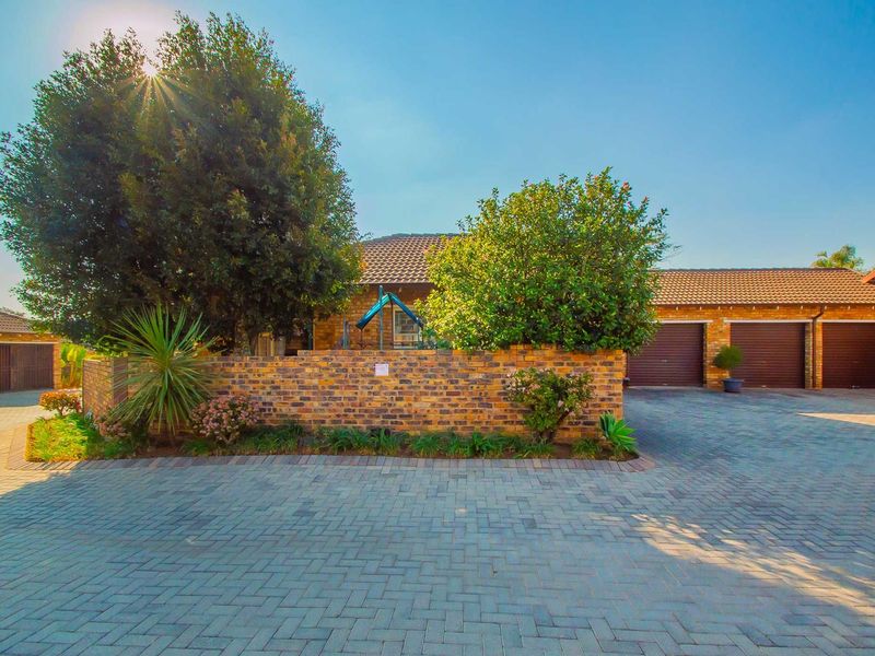 Front exterior view of a townhouse featuring a paved driveway, triple garage doors, and a face brick boundary wall.