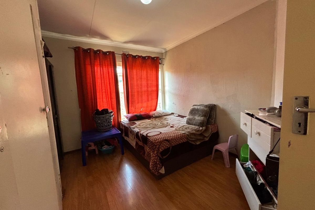 A bedroom featuring laminate flooring and a window with curtain tracks, requiring cosmetic updates to improve the overall aesthetic.