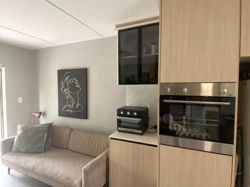 An open-plan living area featuring modern light wood cabinetry, a built-in oven, and neutral tiled flooring, creating a cohesive and functional space.