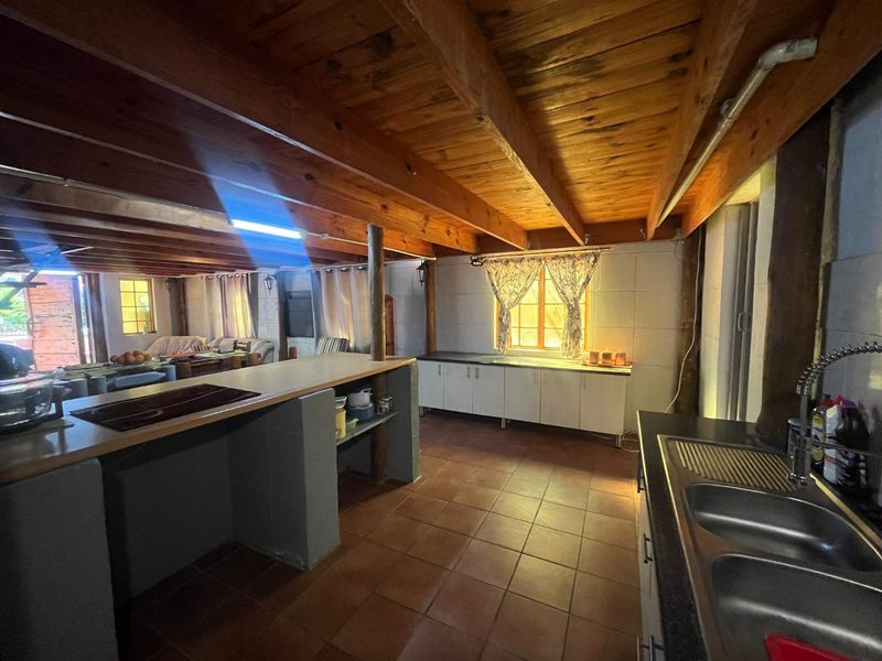Open-plan kitchen and living area featuring exposed timber ceiling beams, tiled flooring, and functional built-in cabinetry with a central island.