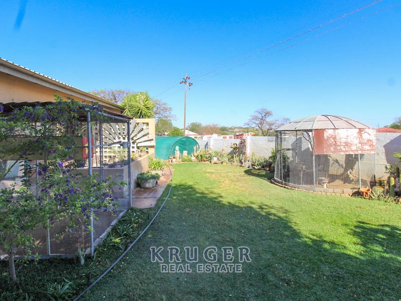 A spacious rear garden featuring a well-maintained lawn, a covered patio area, and perimeter boundary walls.